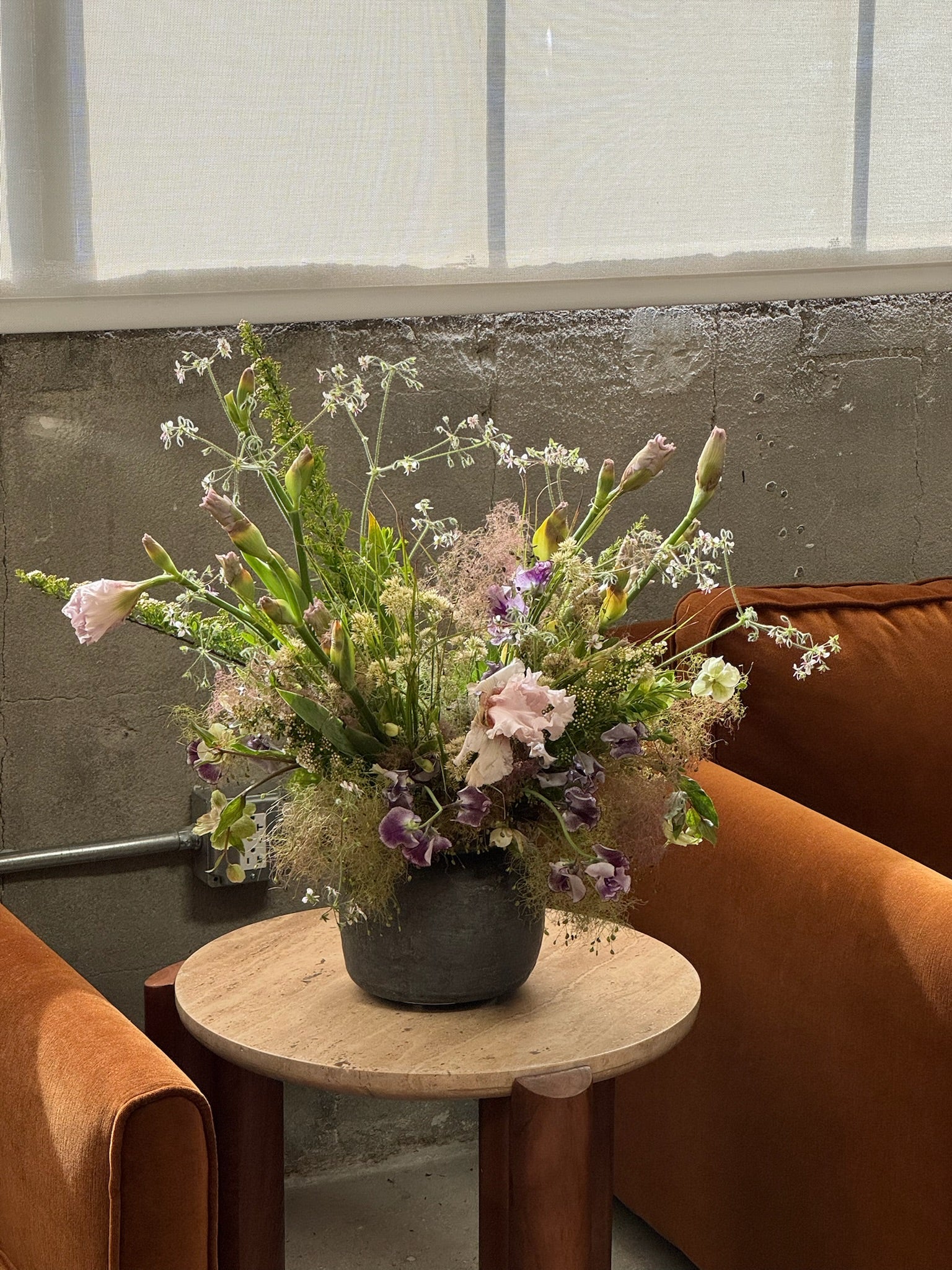 Floral arrangement on a small round table with orange chairs and a concrete wall in the background