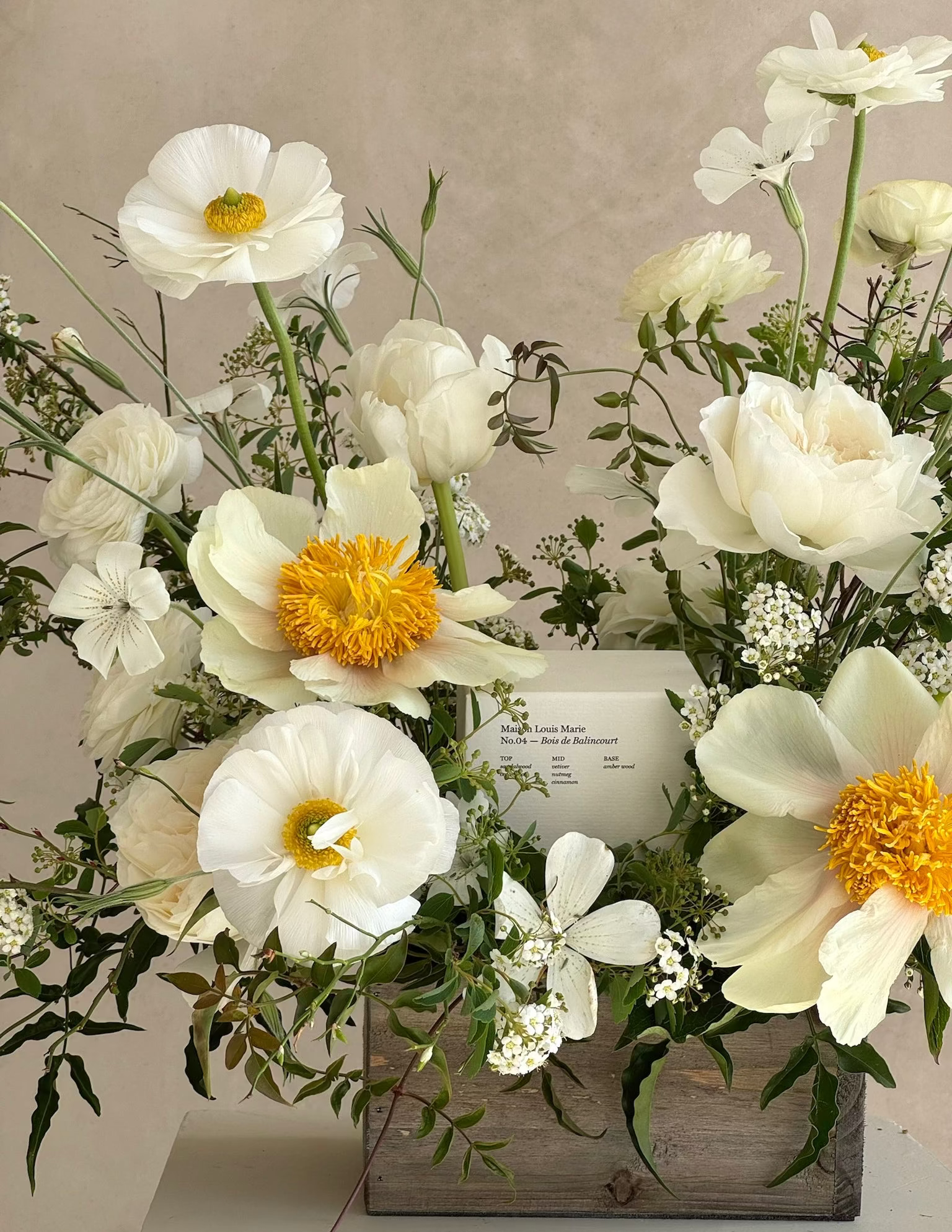Floral arrangement with white and yellow flowers in a wooden box on a neutral background