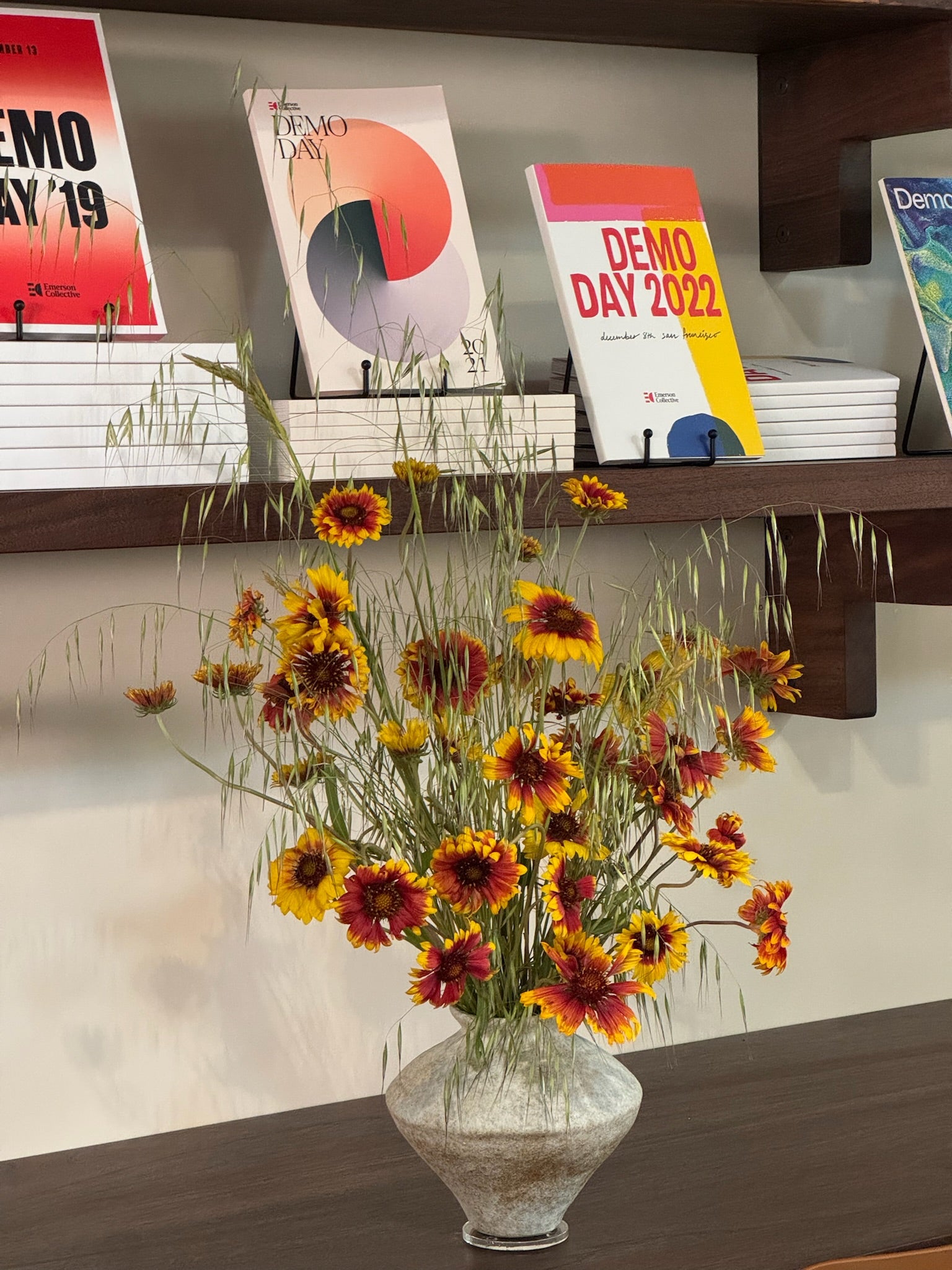 Vase of flowers on a table with books titled 'Demo Day' in the background.