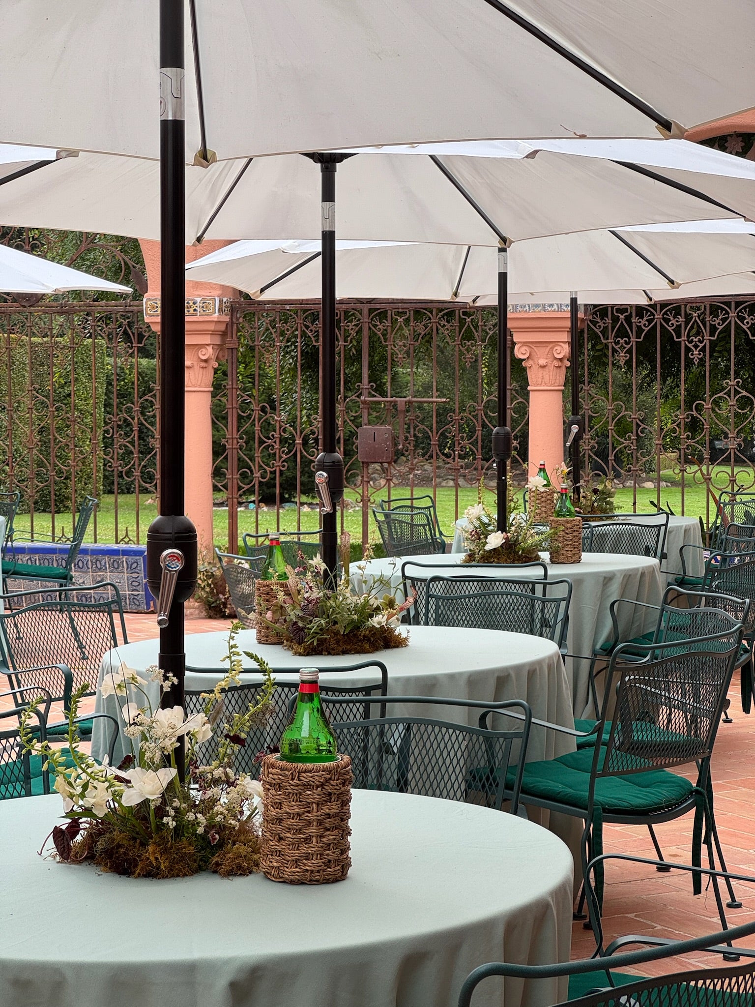 Outdoor setting with tables, chairs, and umbrellas in a garden or courtyard.