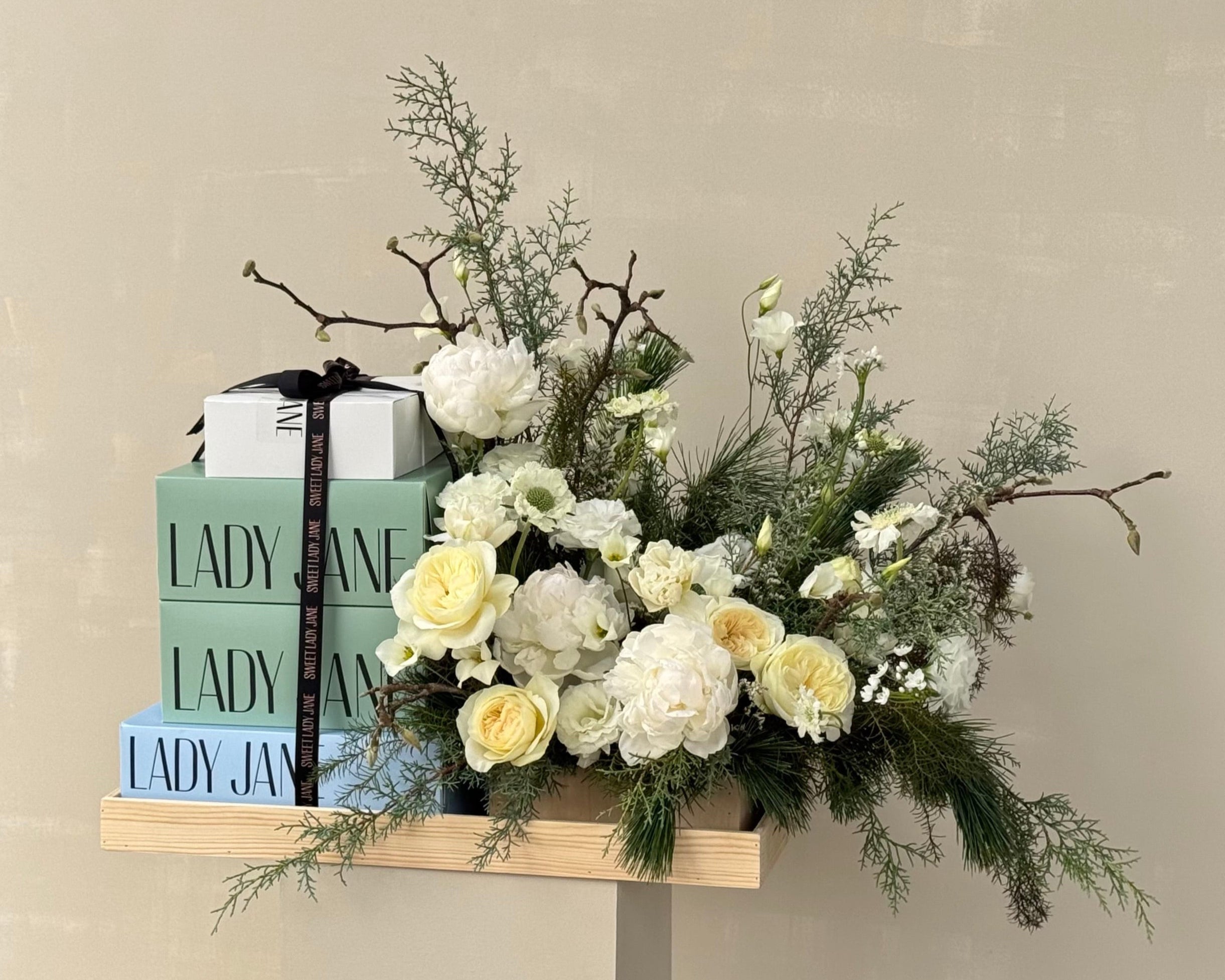 Floral arrangement with greenery and white flowers on a wooden shelf against a beige background