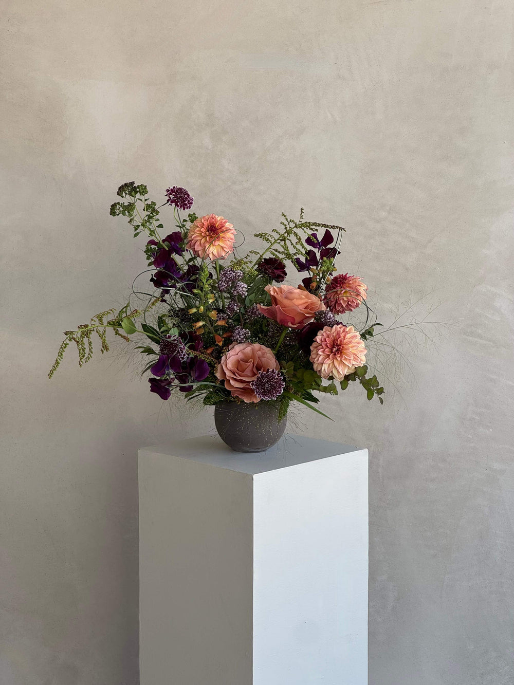 Floral arrangement in a vase on a white pedestal against a plain background