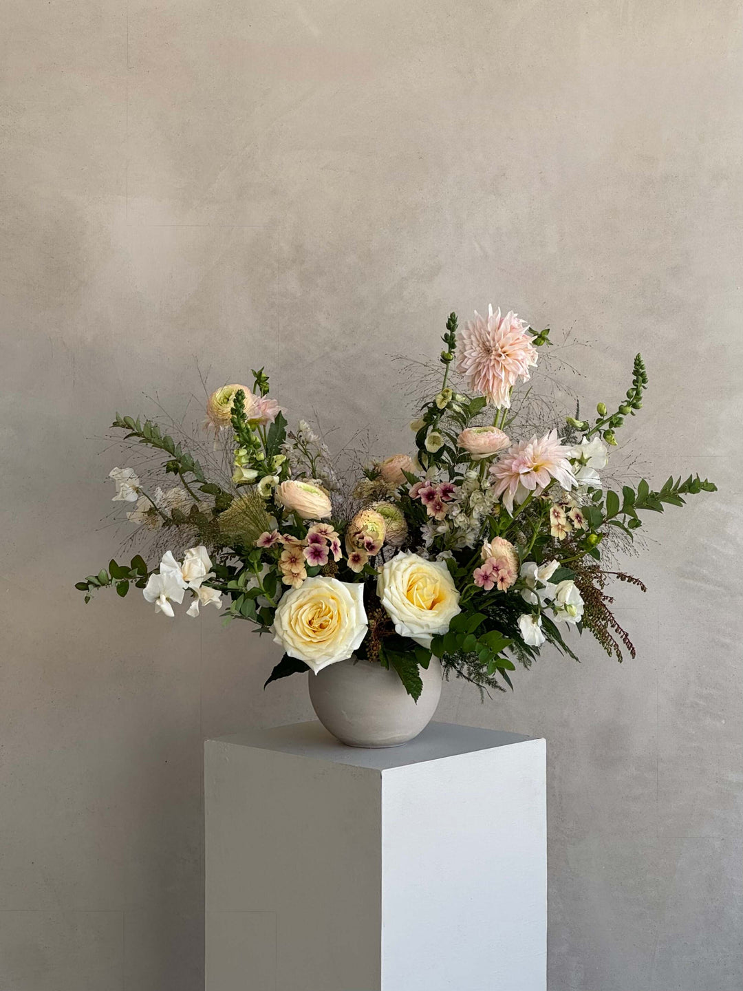 Floral arrangement in a white vase on a gray pedestal against a plain background