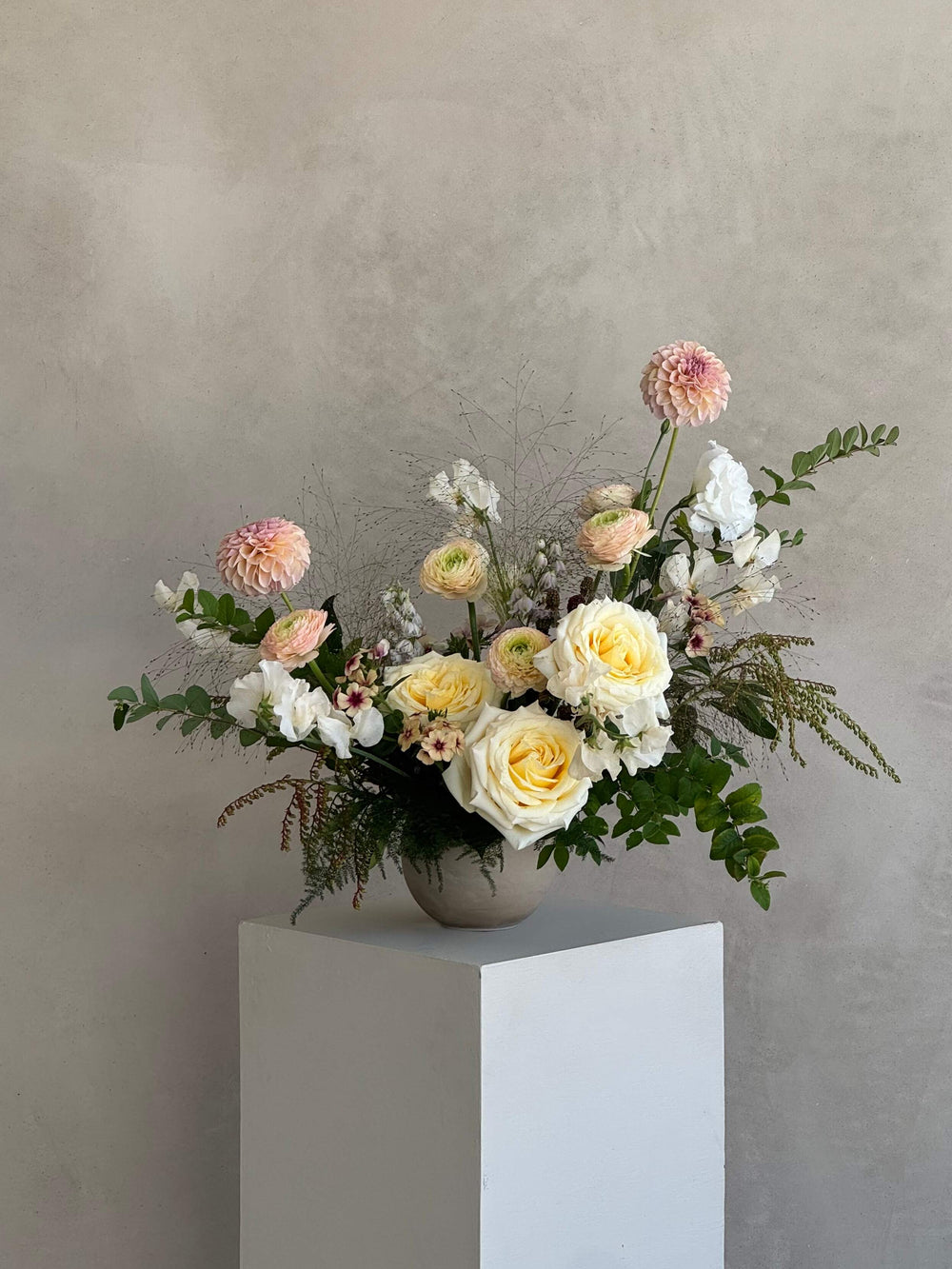 Floral arrangement on a white pedestal against a plain background