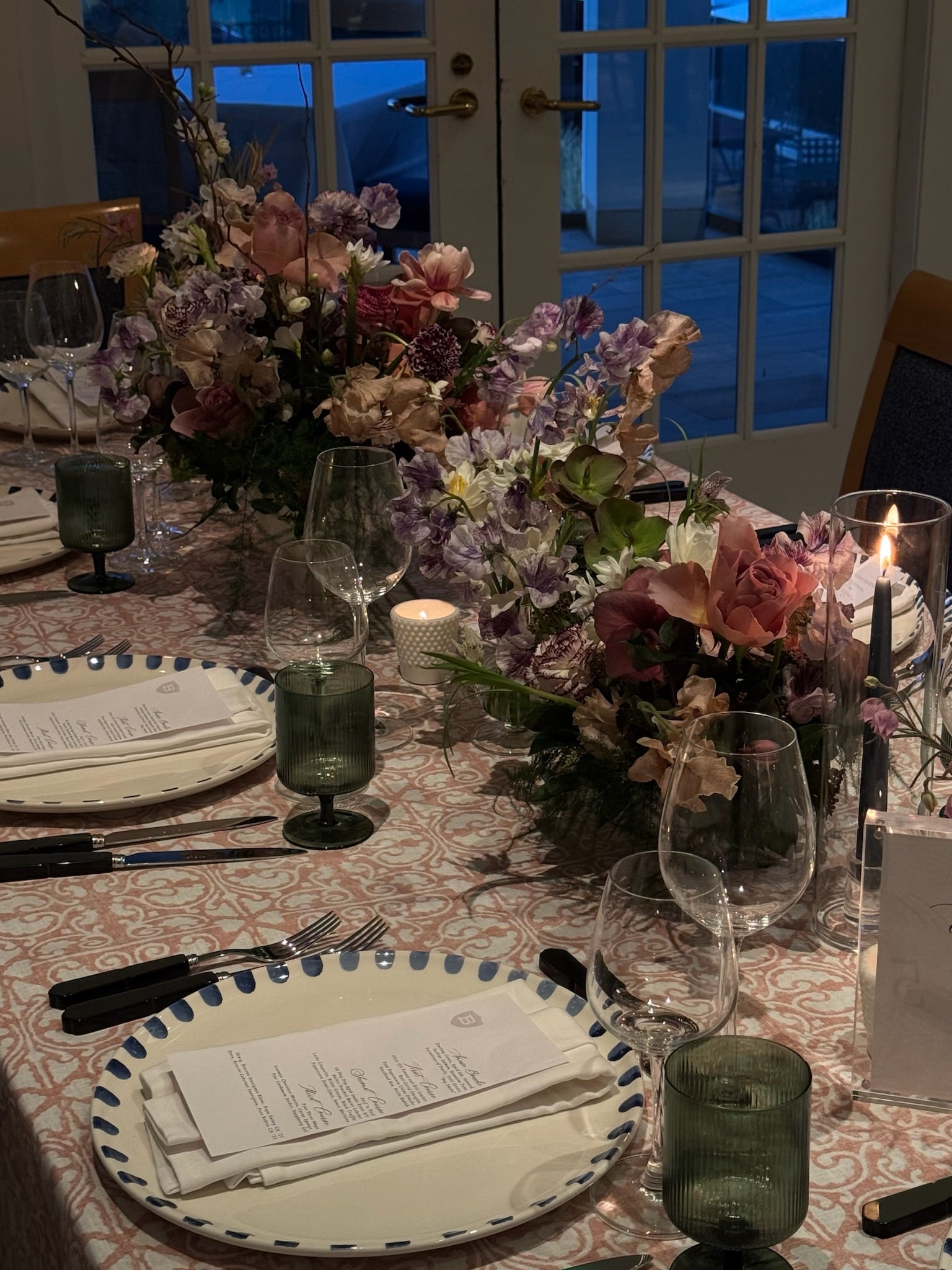 Dining table set for a meal with floral arrangements, candles, and place settings.