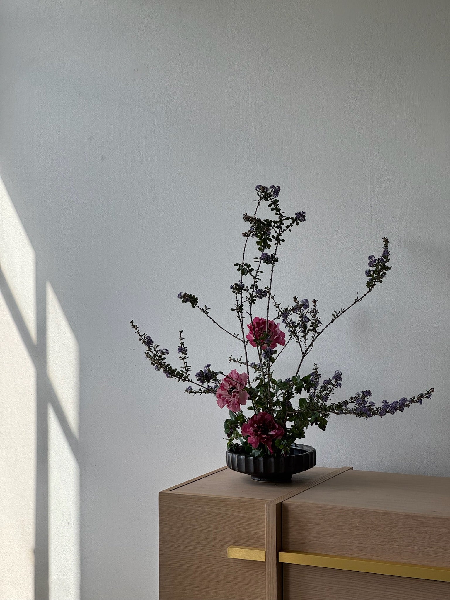 Floral arrangement in a pot on a wooden surface with a light gray background