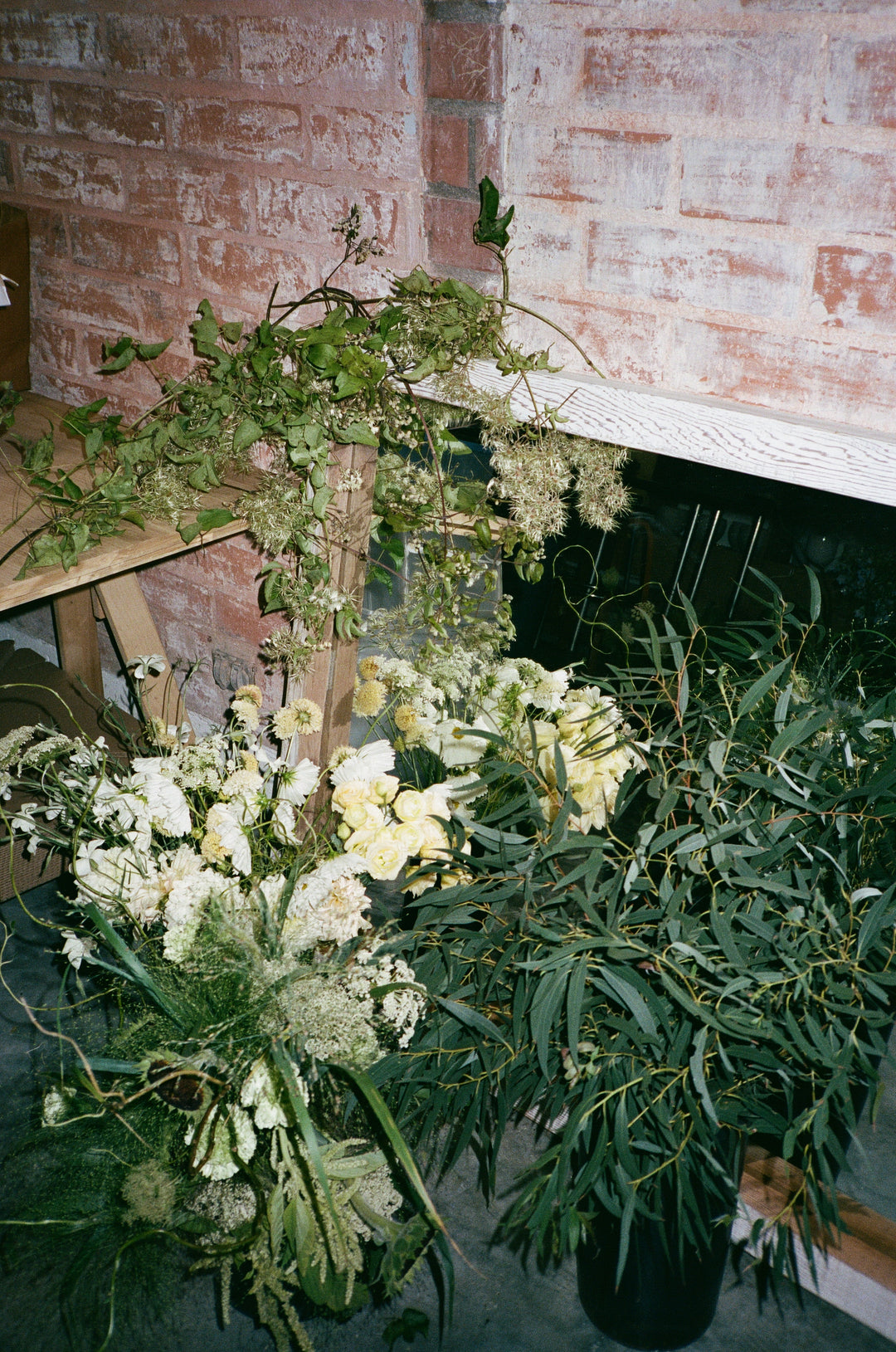 Floral arrangement with white flowers and greenery on a stone surface next to a brick wall.
