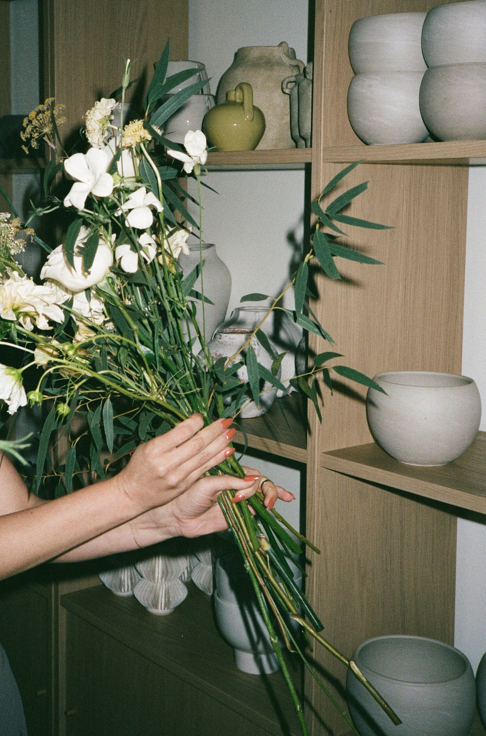 Person arranging flowers with a shelf and decorative items in the background