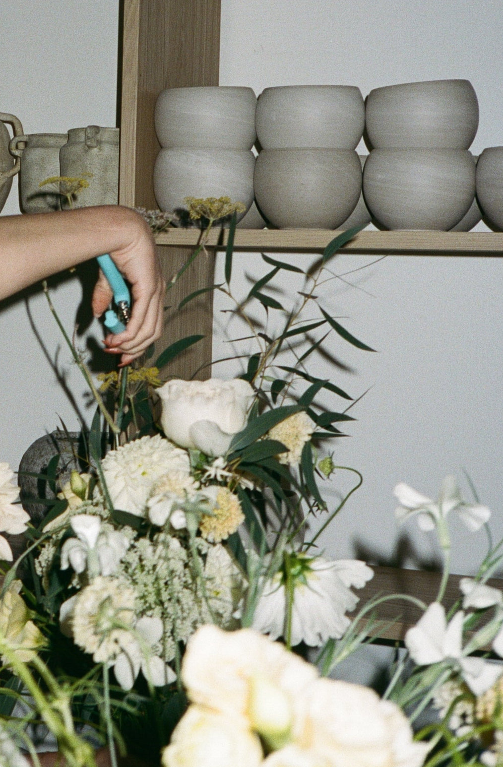 Person arranging flowers with stacked ceramic pots in the background