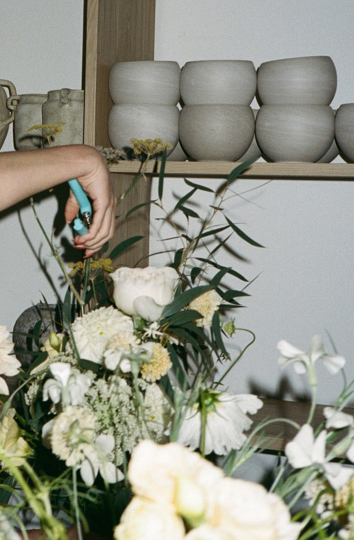 Person arranging flowers with stacked ceramic pots in the background