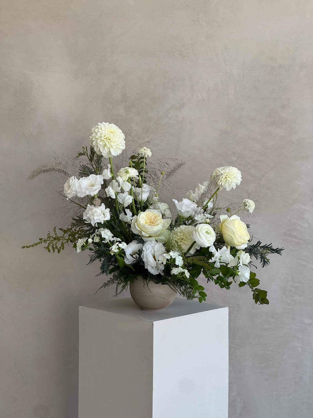 Bouquet of white flowers in a vase on a white pedestal against a beige background
