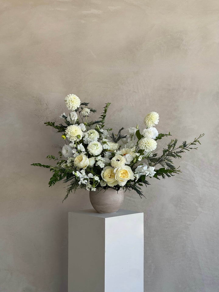 Floral arrangement in a vase on a white pedestal against a beige wall