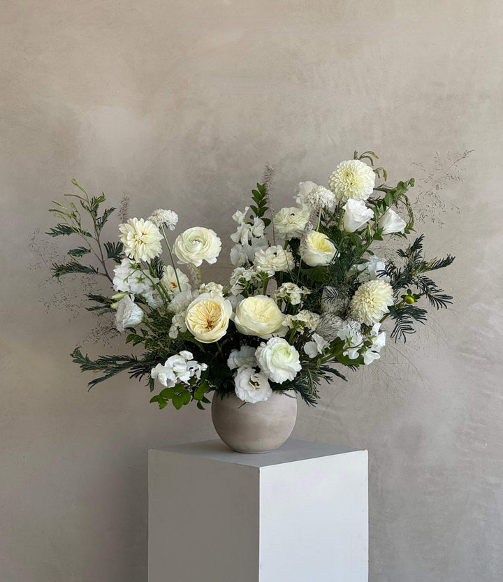 Bouquet of white flowers in a vase on a white pedestal against a beige wall